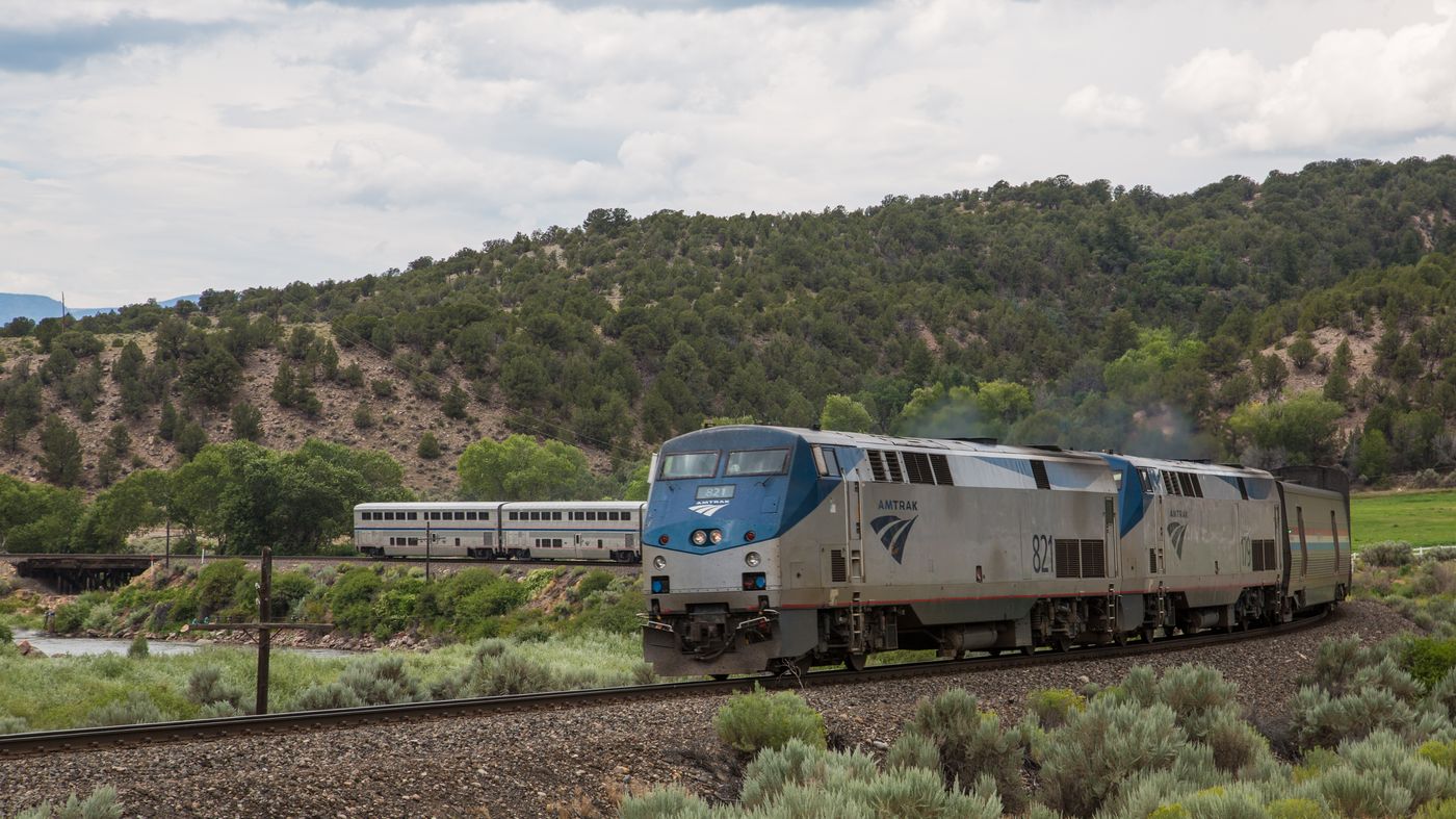 An Amtrak train winding past red rock cliffs and water